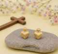 two heart shaped earring studs, on a rock, with a yellow background and a cross with flowers in the back