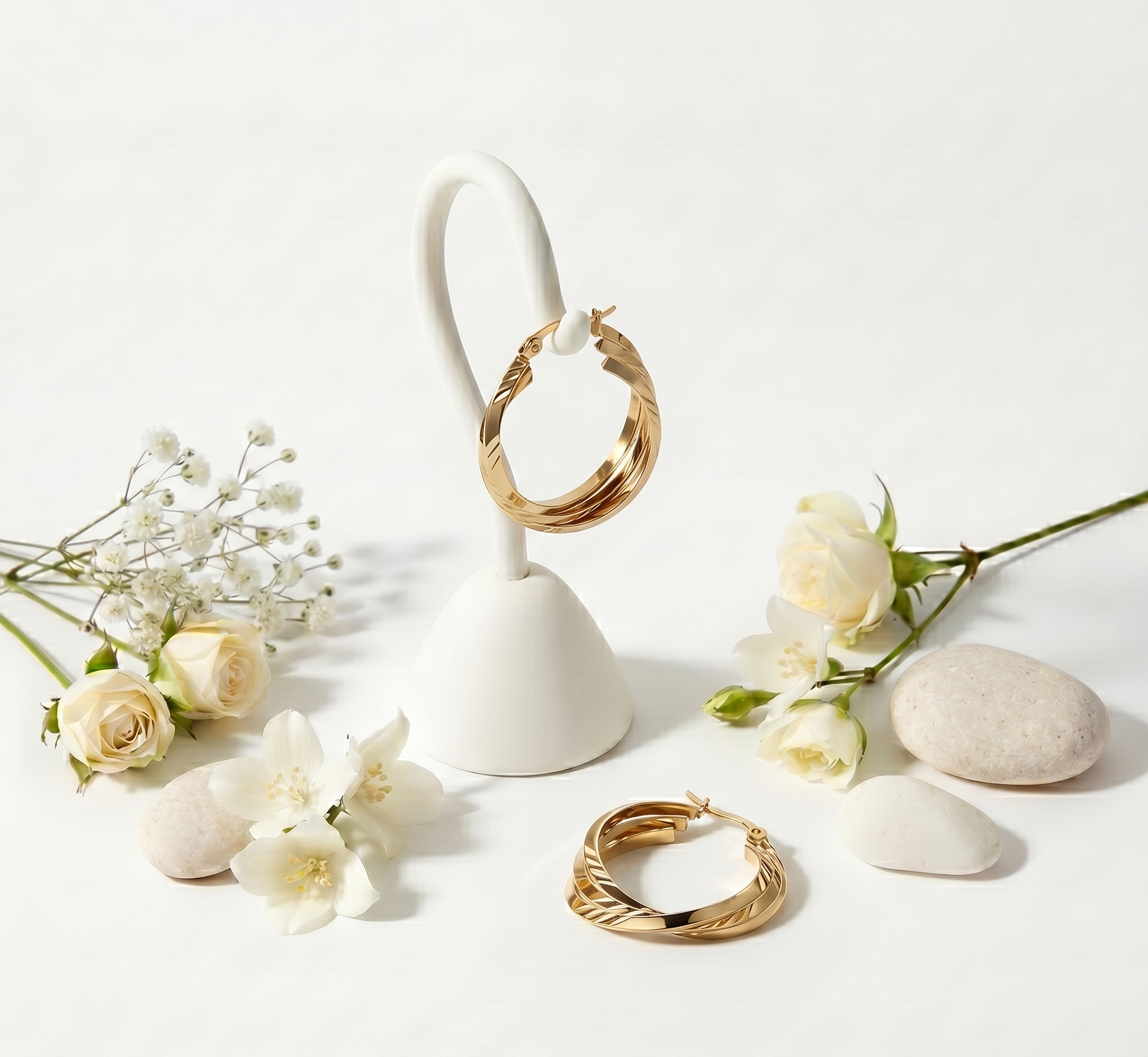 Gold hoop earrings on a white stand with flowers on a light background