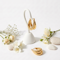 Gold hoop earrings on a white stand with flowers and stones on a light background
