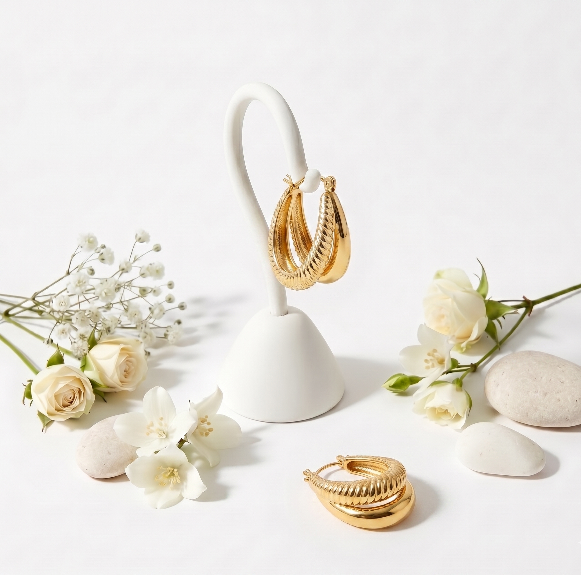 Gold hoop earrings on a white stand with flowers and stones on a light background