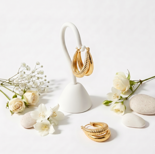 Gold hoop earrings on a white stand with flowers and stones on a light background