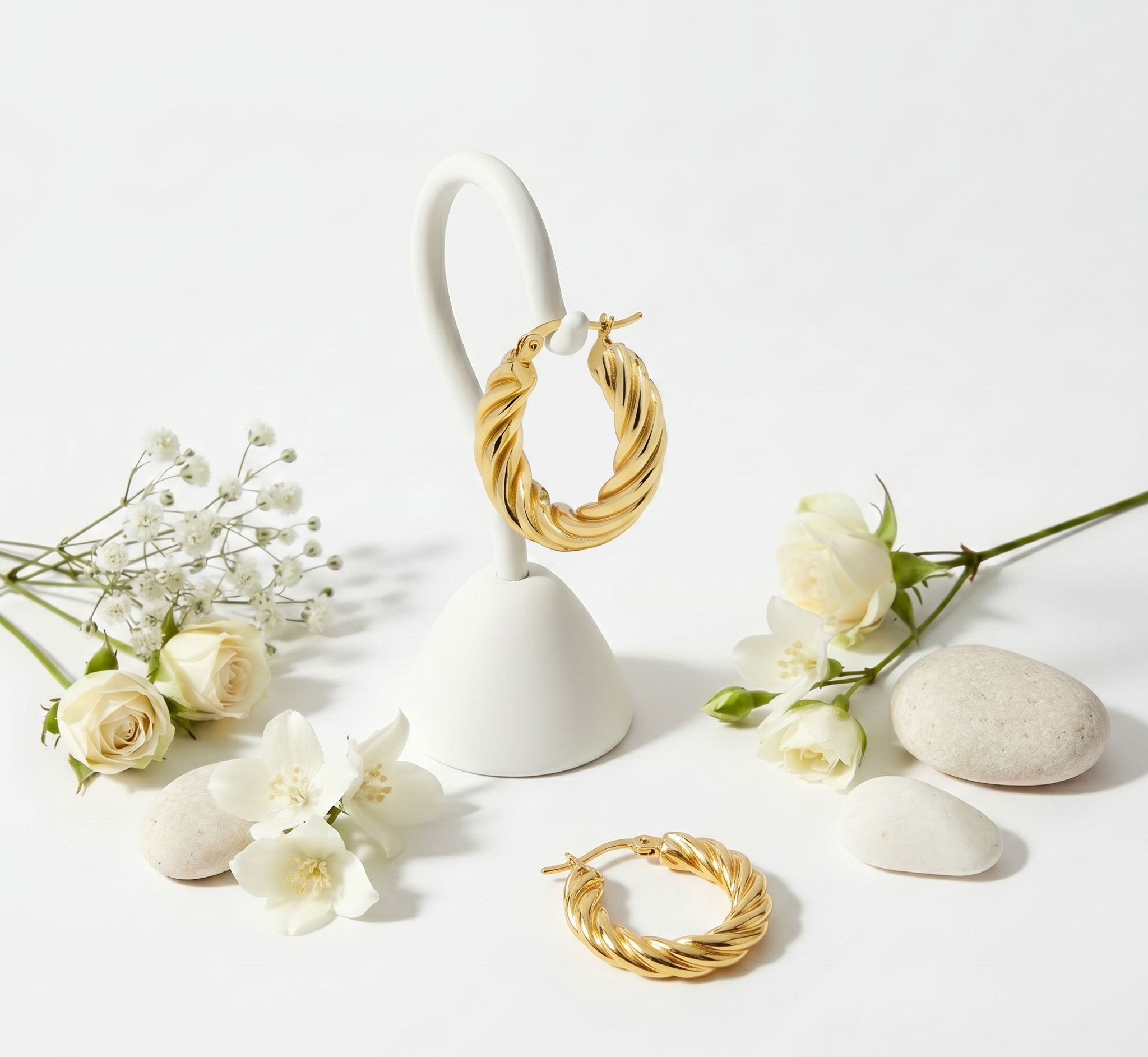 Gold hoop earrings on a white stand with white flowers on a light gray background