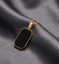 Gold necklace with a black pendant on a gray fabric background