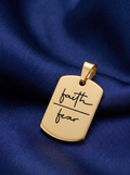 Gold pendant with 'faith' and 'fear' engraved on a blue fabric background