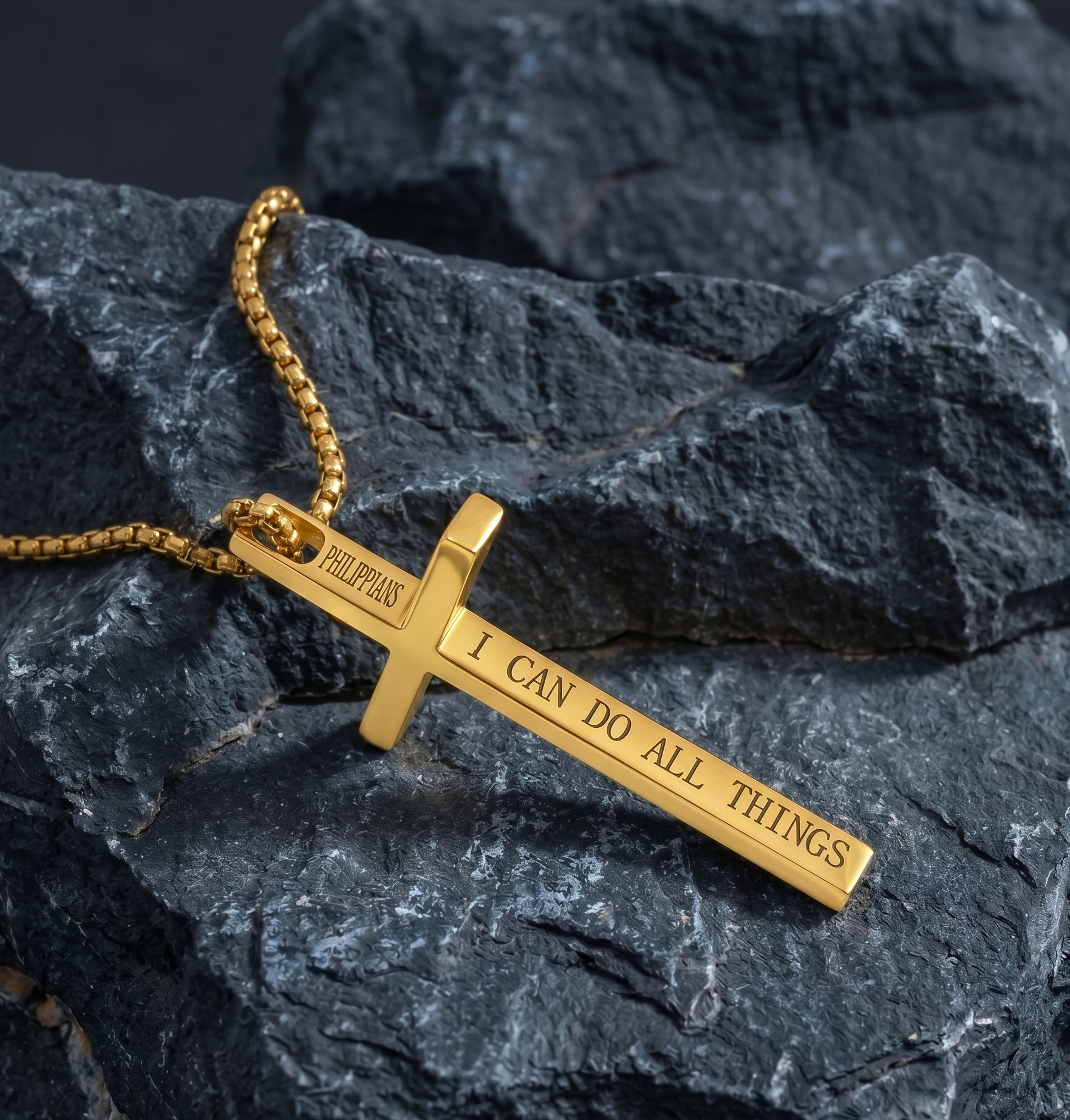 Gold cross necklace with engraved text on dark stone background