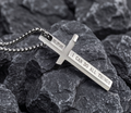 Silver cross pendant with engraved text on a rocky surface