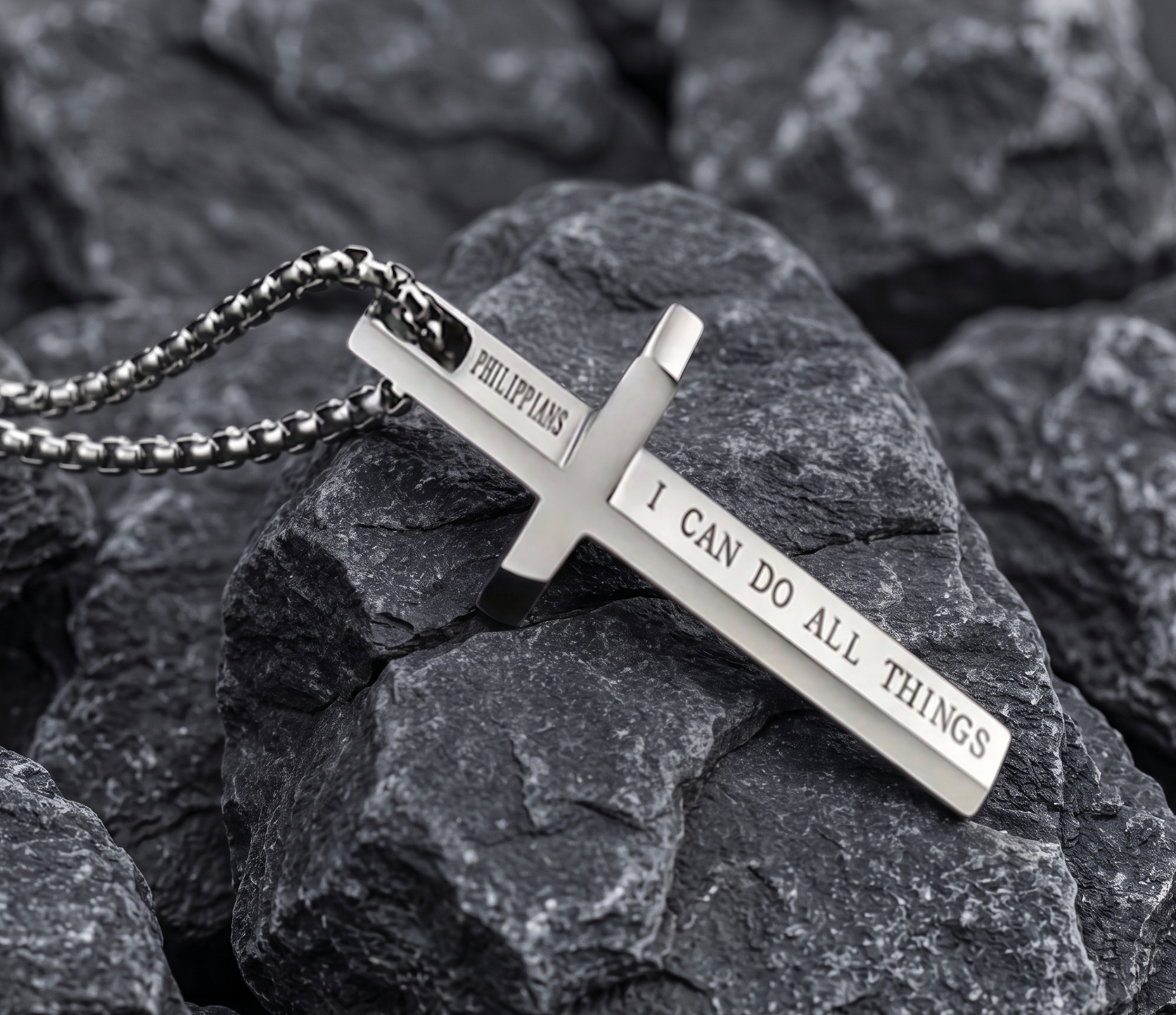 Silver cross pendant with engraved text on a rocky surface
