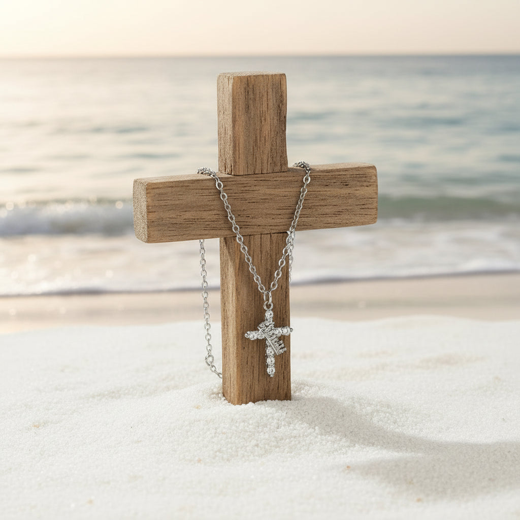 a cross embedded in beach sand, with a silver necklace chain and cross hanging on the wooden cross, oceanic backgorund