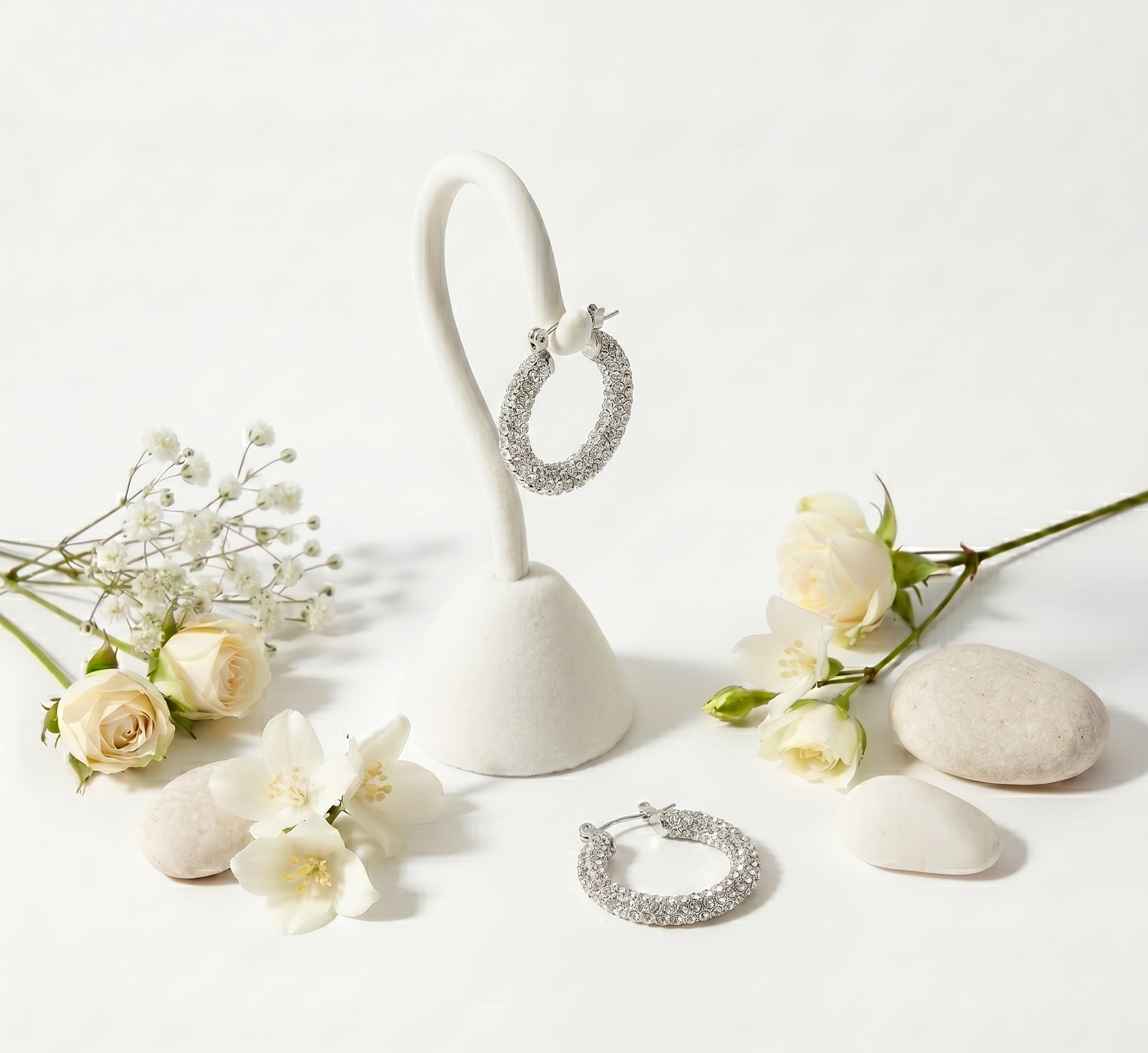 Silver hoop earrings on a white stand with white flowers on a light background
