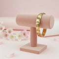 Gold bracelet on a pink stand with a soft pink background and flowers.