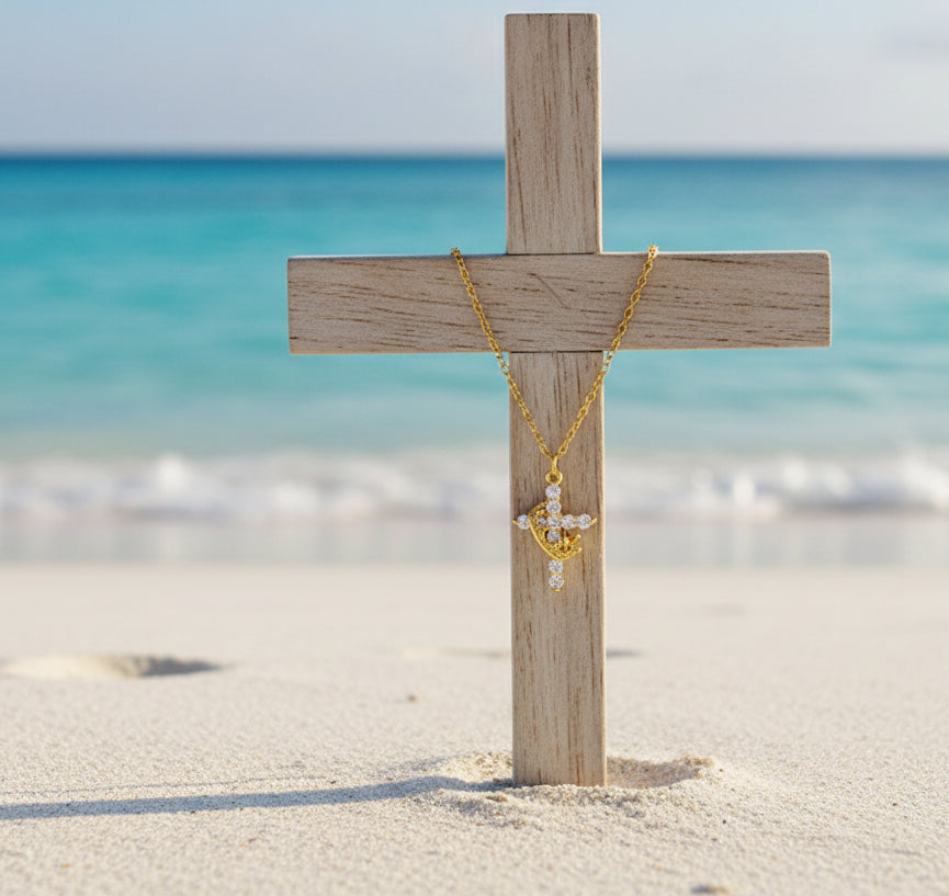 a cross embedded in beach sand, with a gold necklace chain and cross hanging on the wooden cross, oceanic backgorund