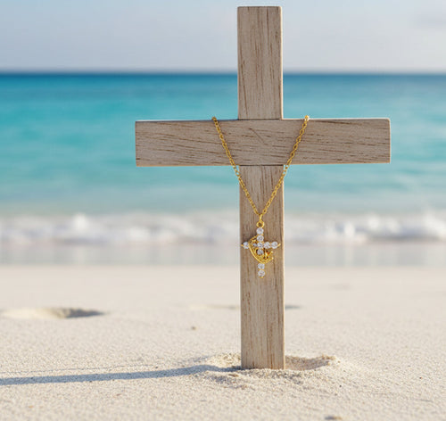 a cross embedded in beach sand, with a gold necklace chain and cross hanging on the wooden cross, oceanic backgorund
