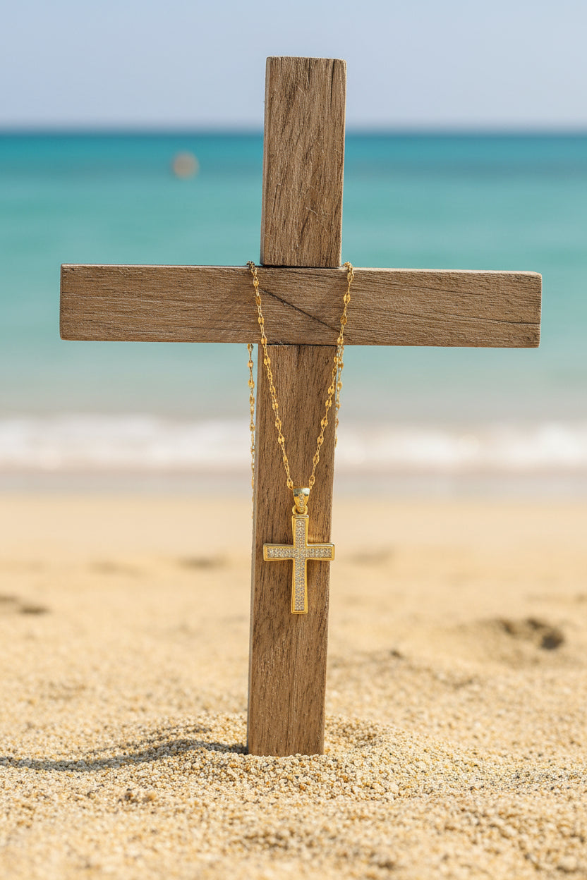 a cross embedded in beach sand, with a golden necklace chain and cross hanging on the wooden cross, oceanic backgorund