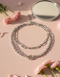 silver necklace, chain, with pale pink background, mirror and flowers on surface