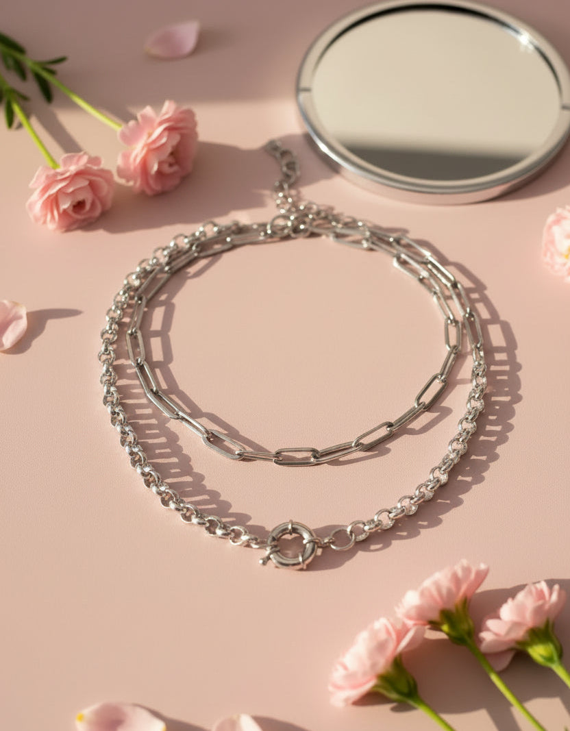 silver necklace, chain, with pale pink background, mirror and flowers on surface