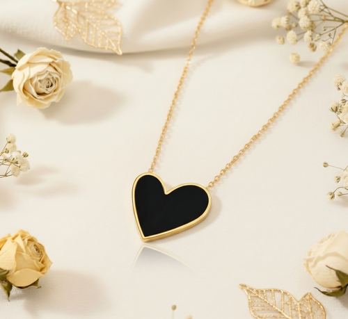 Gold necklace with a black heart pendant on a light background with flowers