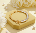 Gold bracelet with clear stones on a yellow stand with white flowers