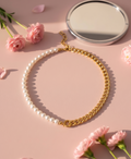 Gold chain necklace with pearl accents on a pink surface with flowers and a mirror.