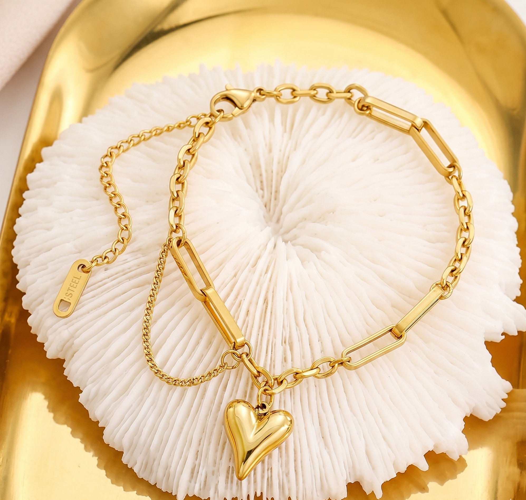 Gold bracelet with a heart charm on a white shell against a gold background