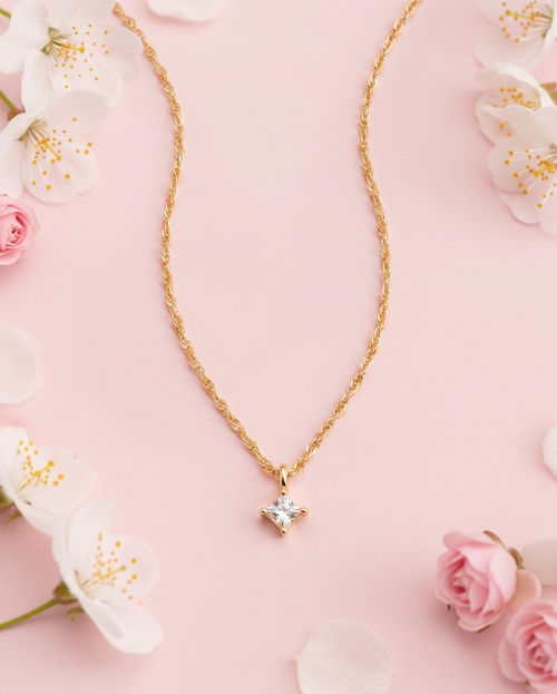 Gold necklace with a diamond pendant on a pink background with flowers