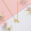 Gold double disc necklace on pink and white background