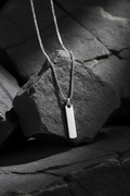 Silver necklace with a rectangular pendant on a textured black surface.