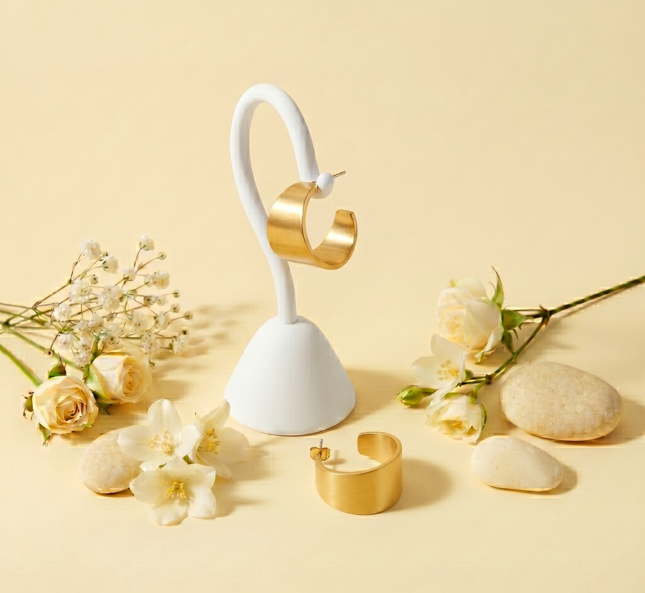 Gold earrings on a white stand with flowers and stones on a beige background