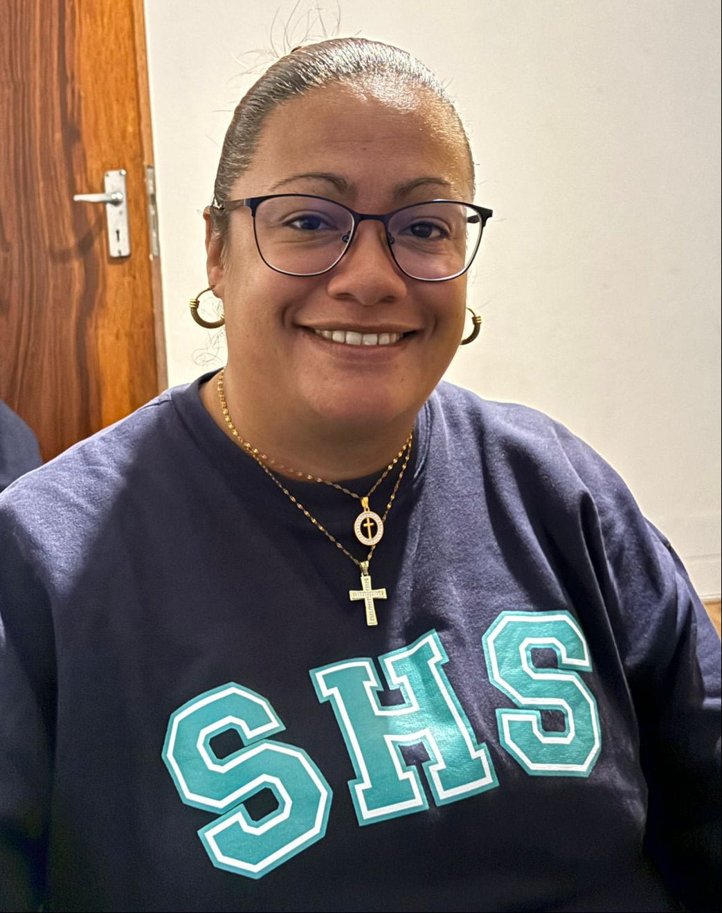Person wearing a dark blue sweatshirt with 'SHS' on it, sitting indoors.