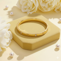 Gold bracelet with small diamonds on a yellow stand with white flowers and pearls.