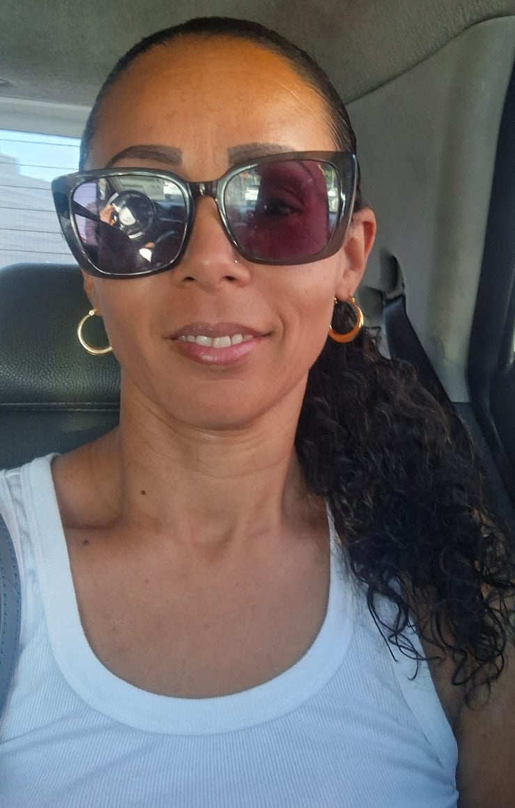 Woman wearing sunglasses and a white tank top inside a vehicle.