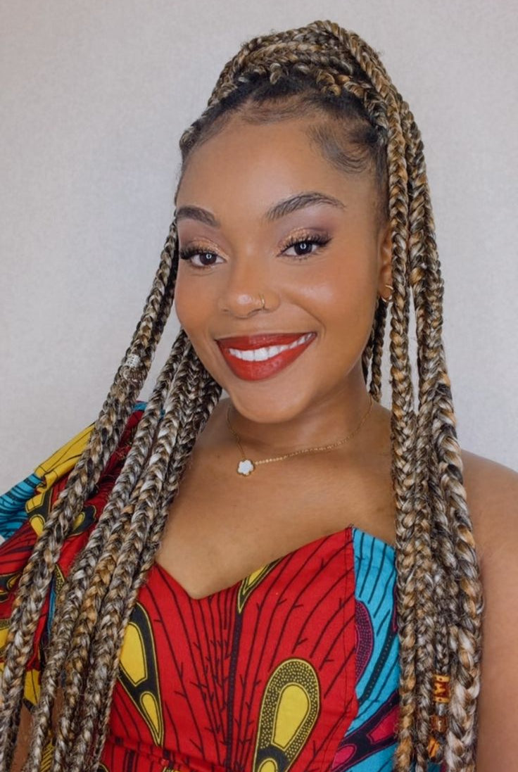 Woman with braided hair wearing a colorful traditional outfit against a plain background