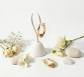 Gold hoop earrings on a white stand with flowers and stones on a light background