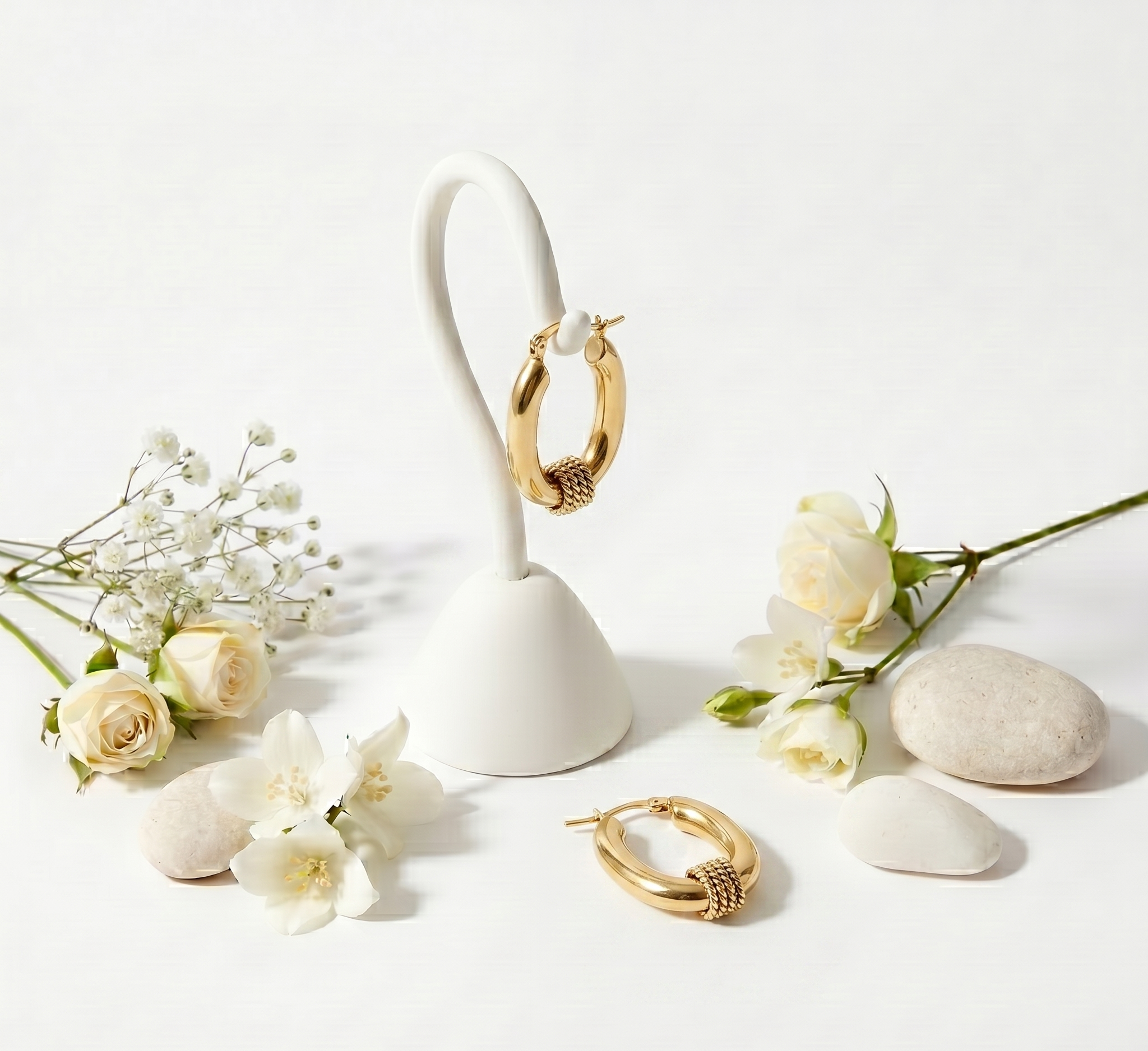 Gold hoop earrings on a white stand with flowers and stones on a light background