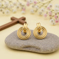 Pair of gold hoop earrings on a yellow background, with flowers and a cross
